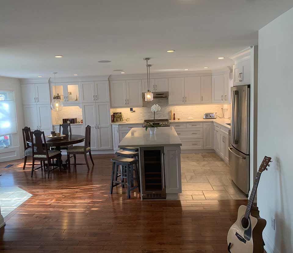 Bright open kitchen and dining area with white cabinets, island, hardwood floors, and guitar at right
