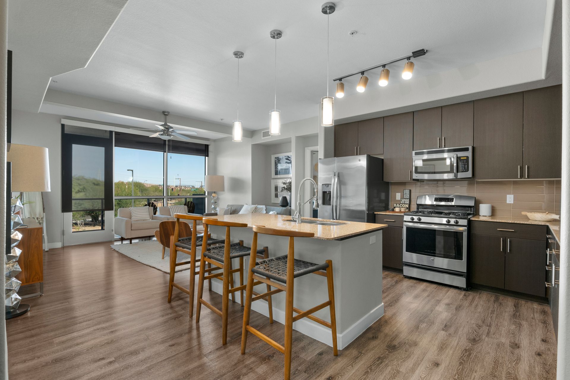 Modern open-concept kitchen and living area with wooden floors, stainless steel appliances, and an island with bar stools.