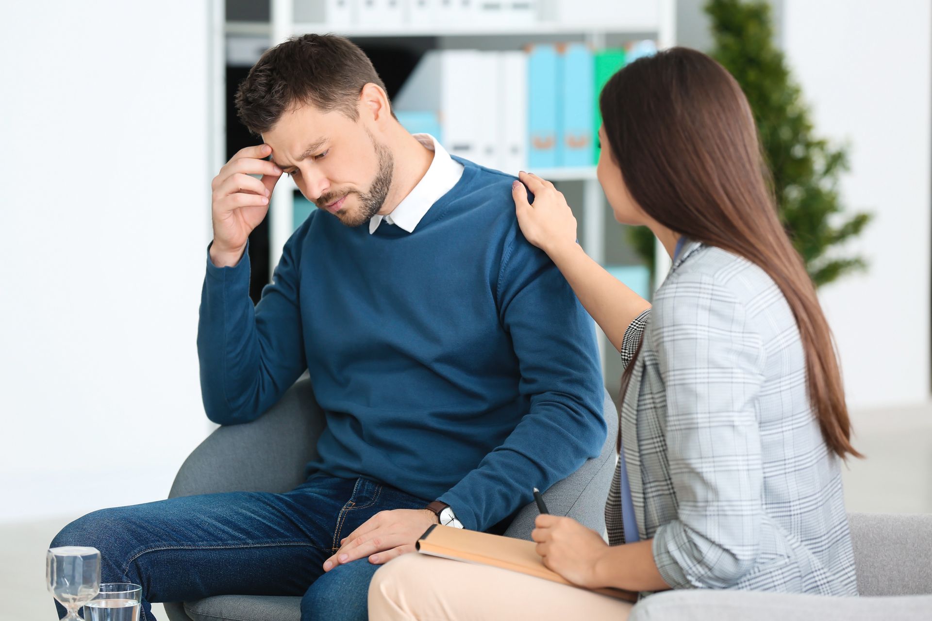 A woman is comforting a man who is sitting on a couch.