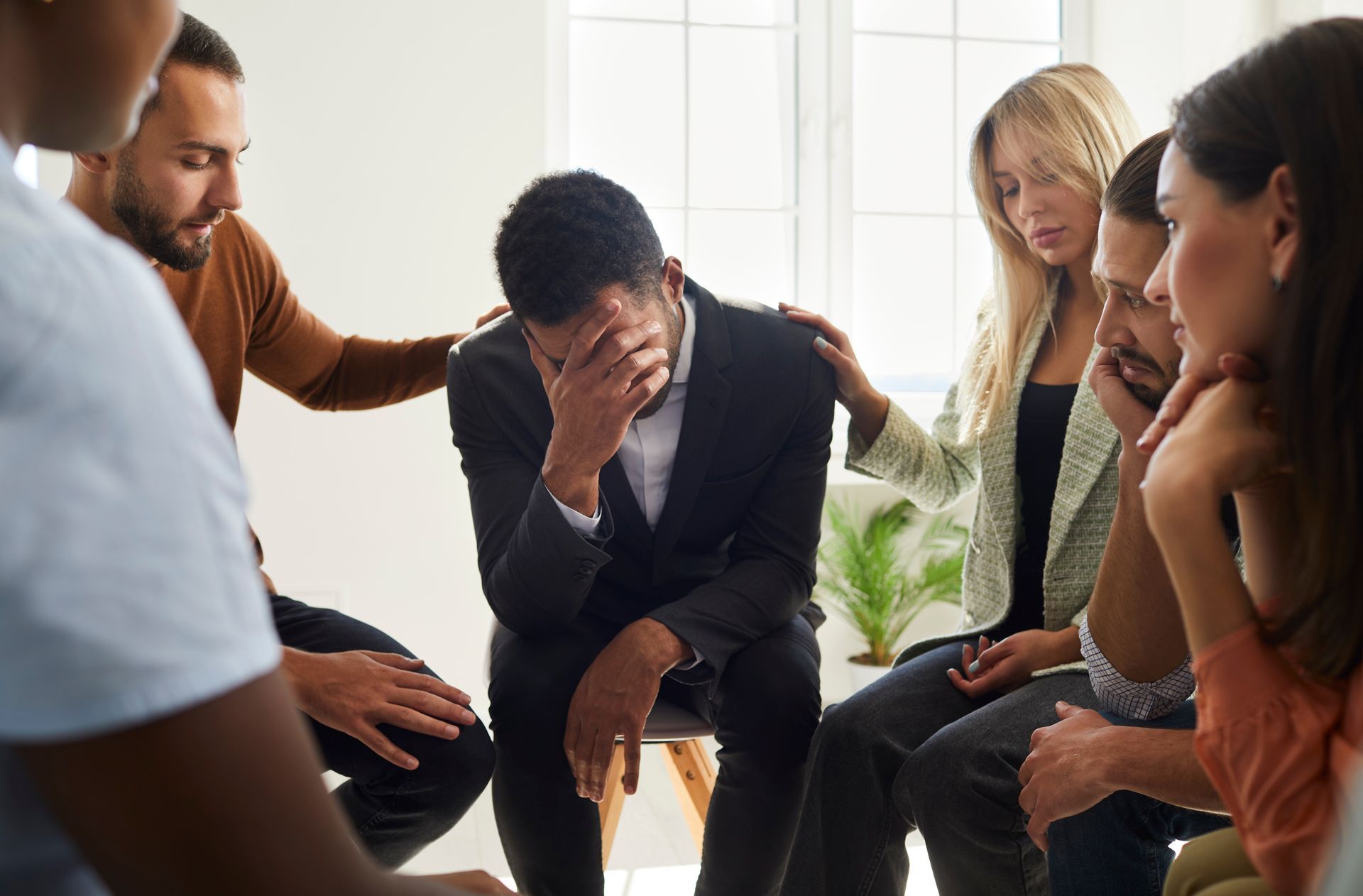A group of people are sitting in a circle with a man covering his face.