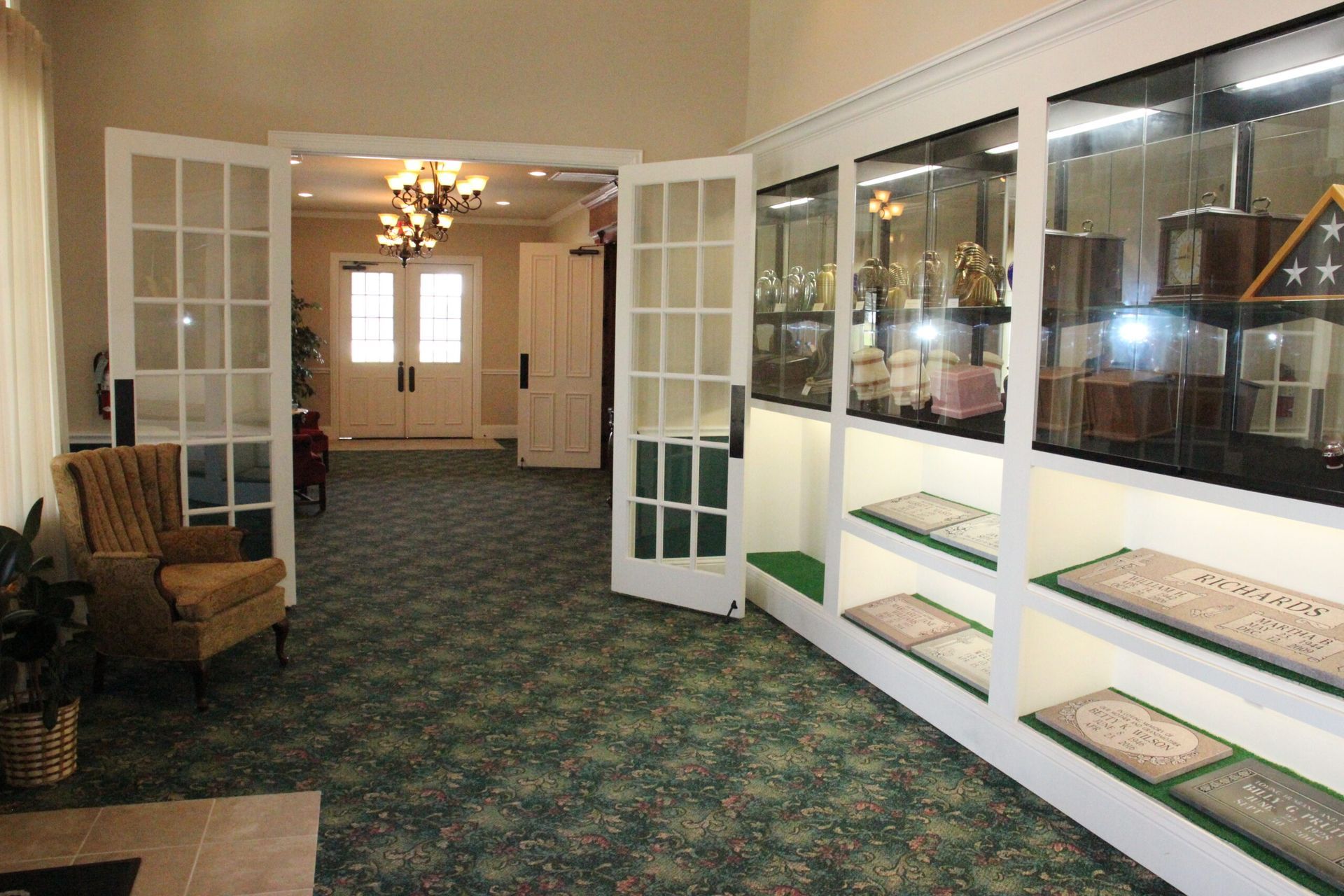 A hallway with a chair and a glass door leading to a display case.