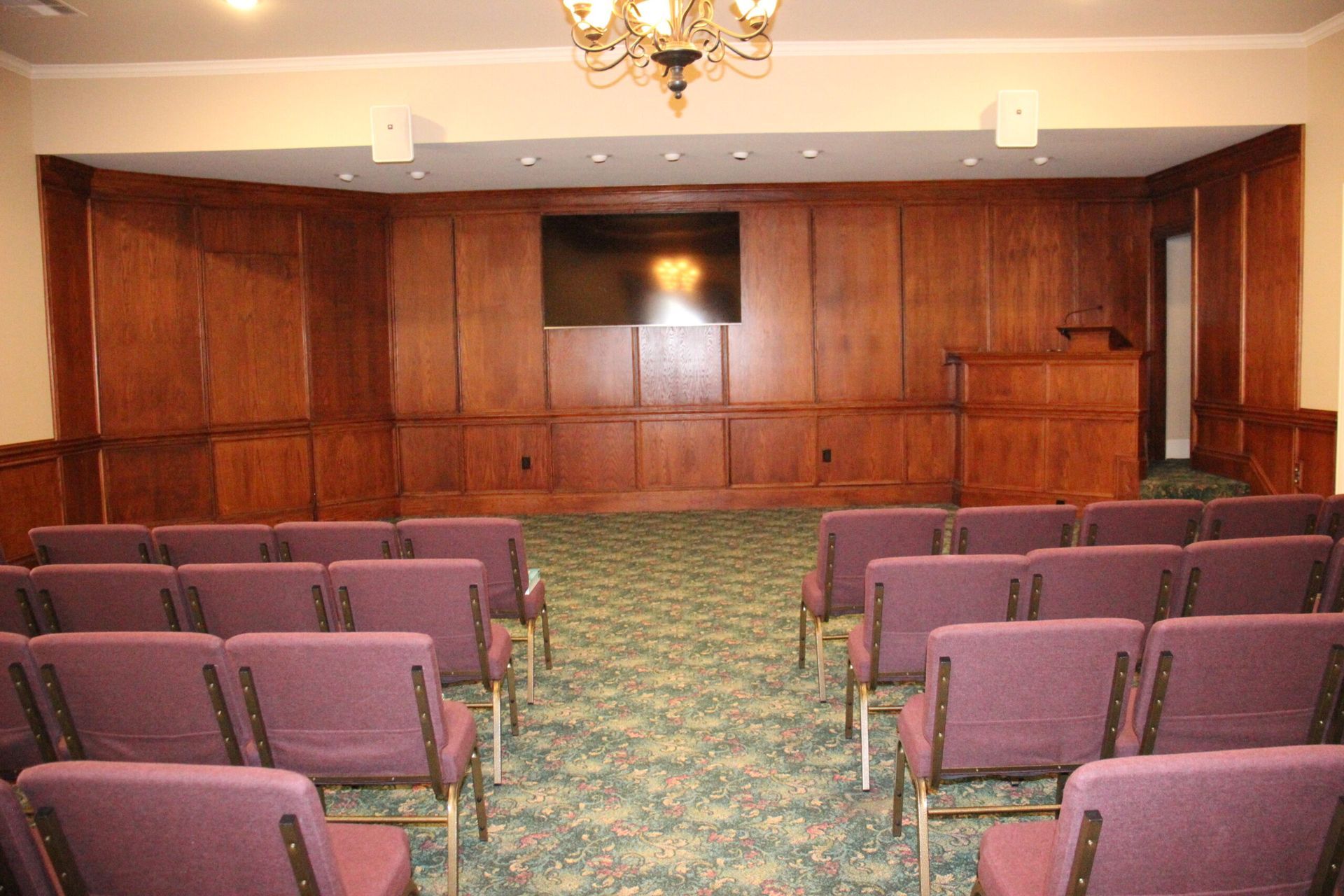 A room with rows of purple chairs and a television on the wall.