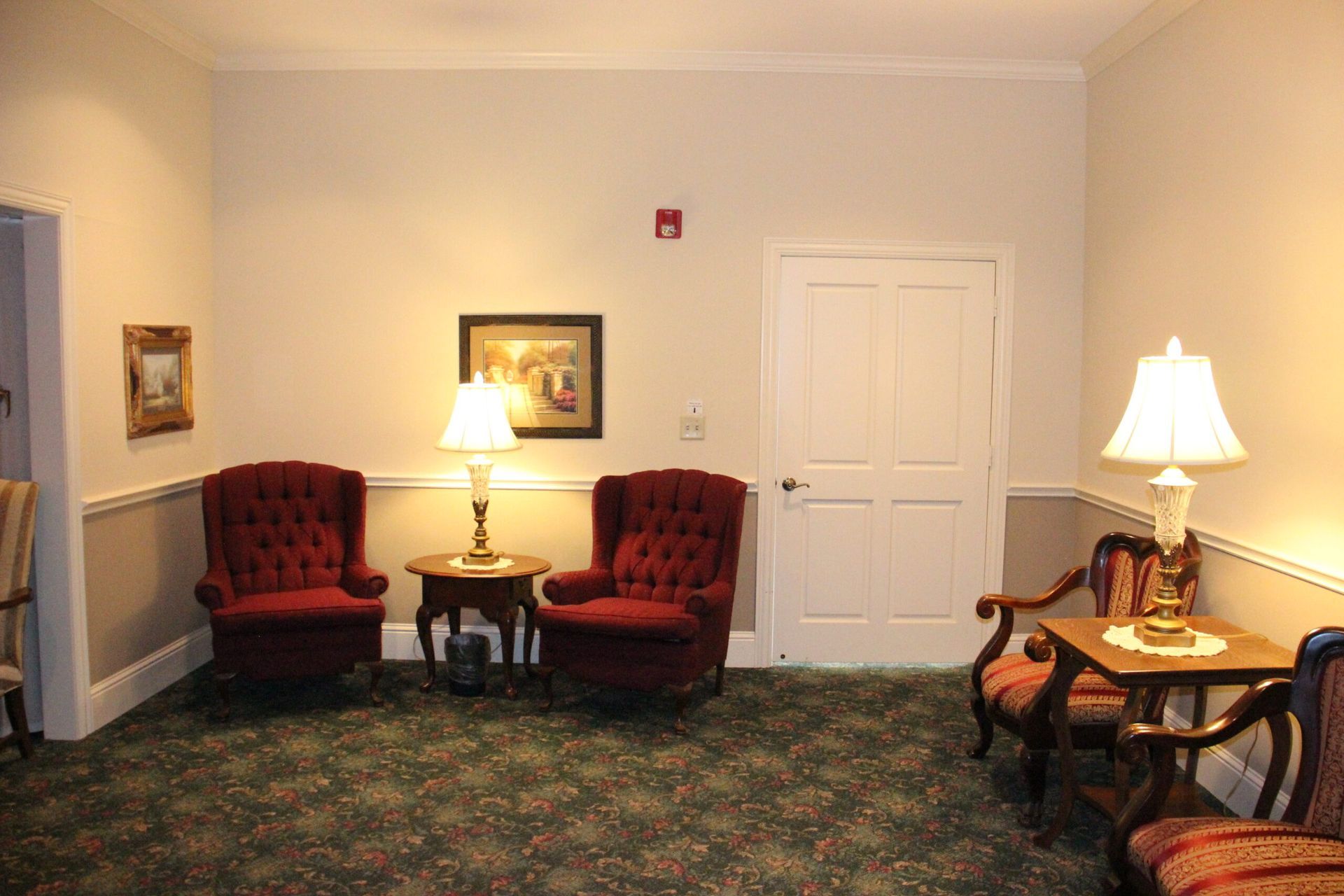 A living room with chairs , tables , lamps and a door.