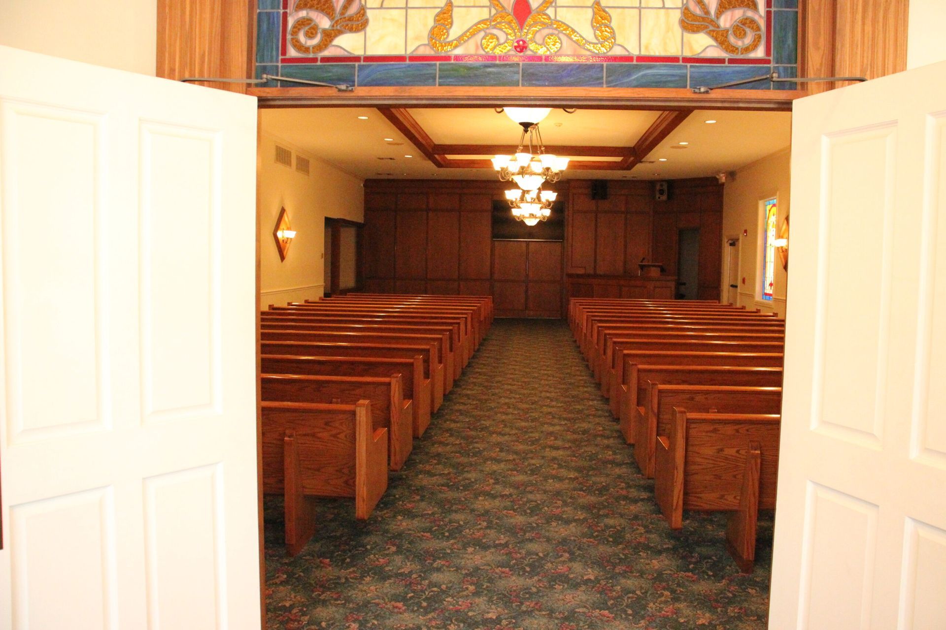 A church with rows of wooden benches and a stained glass window.