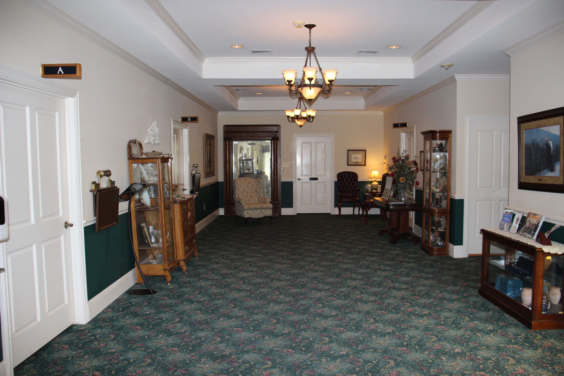 A long hallway with green carpet and a chandelier