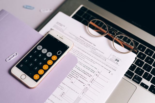 Calculator phone, paperwork, and eyeglasses on a laptop keyboard
