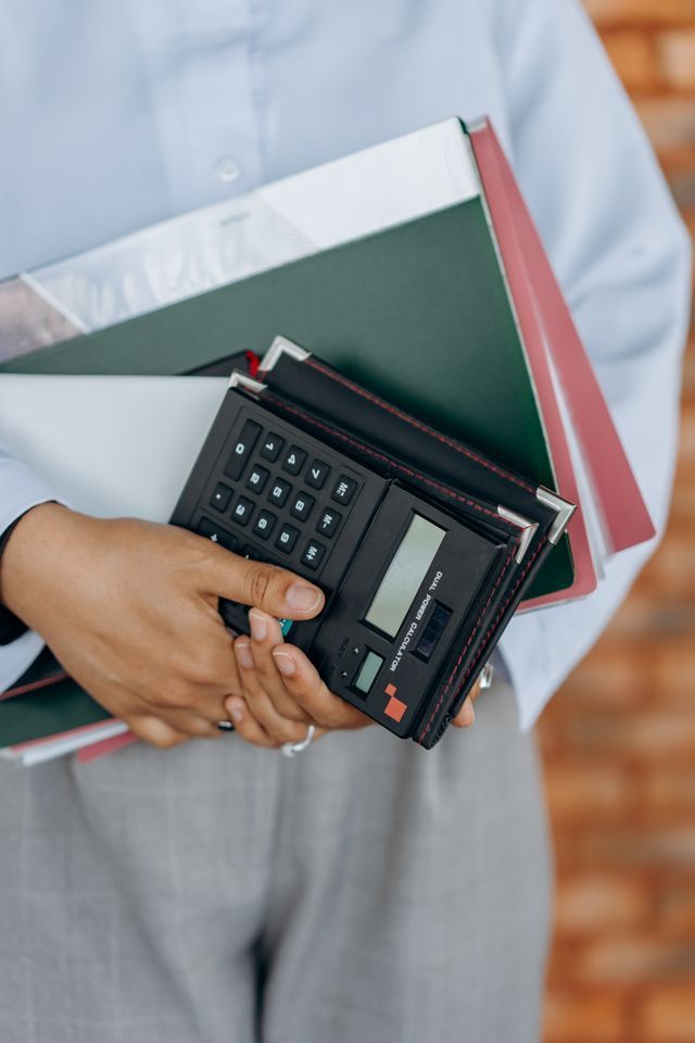 Person holding a calculator and folders against a neutral background