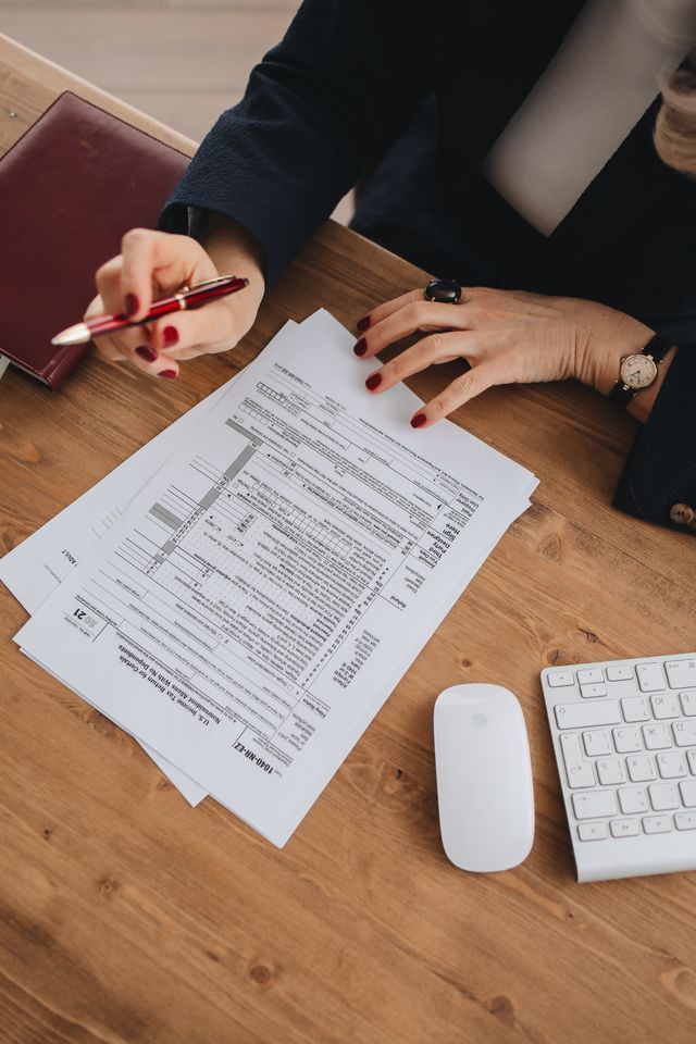 Hands reviewing a document at a desk with a pen, keyboard, and mouse nearby.