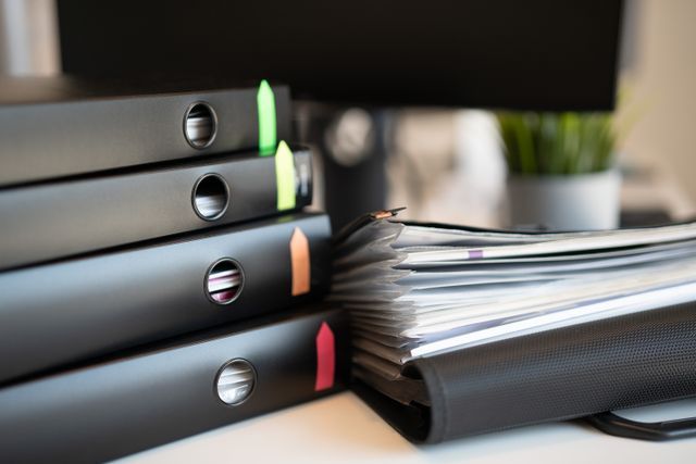 Stacked black binders beside a thick open notebook with colored tabs on a desk