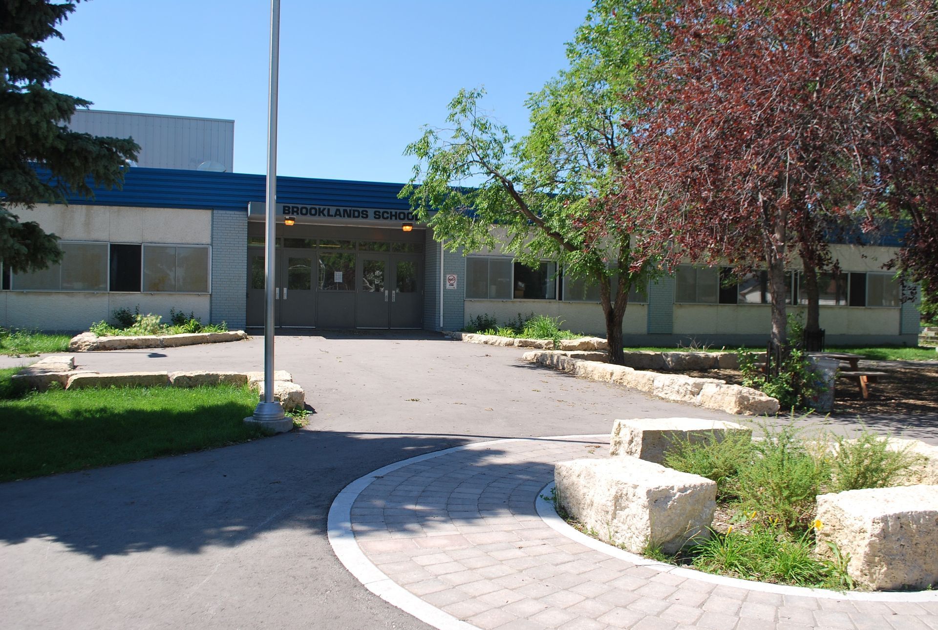 Courtyard entrance to Brooklands Elementary with trees, landscaping, and a paved walkway in bright sunlight