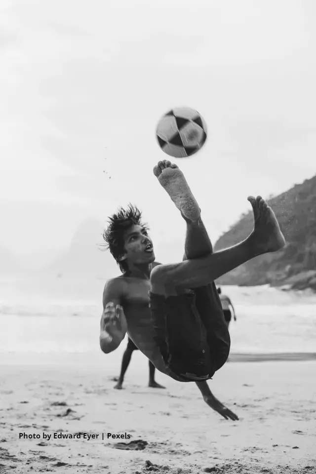 A man is doing a trick with a soccer ball on the beach.