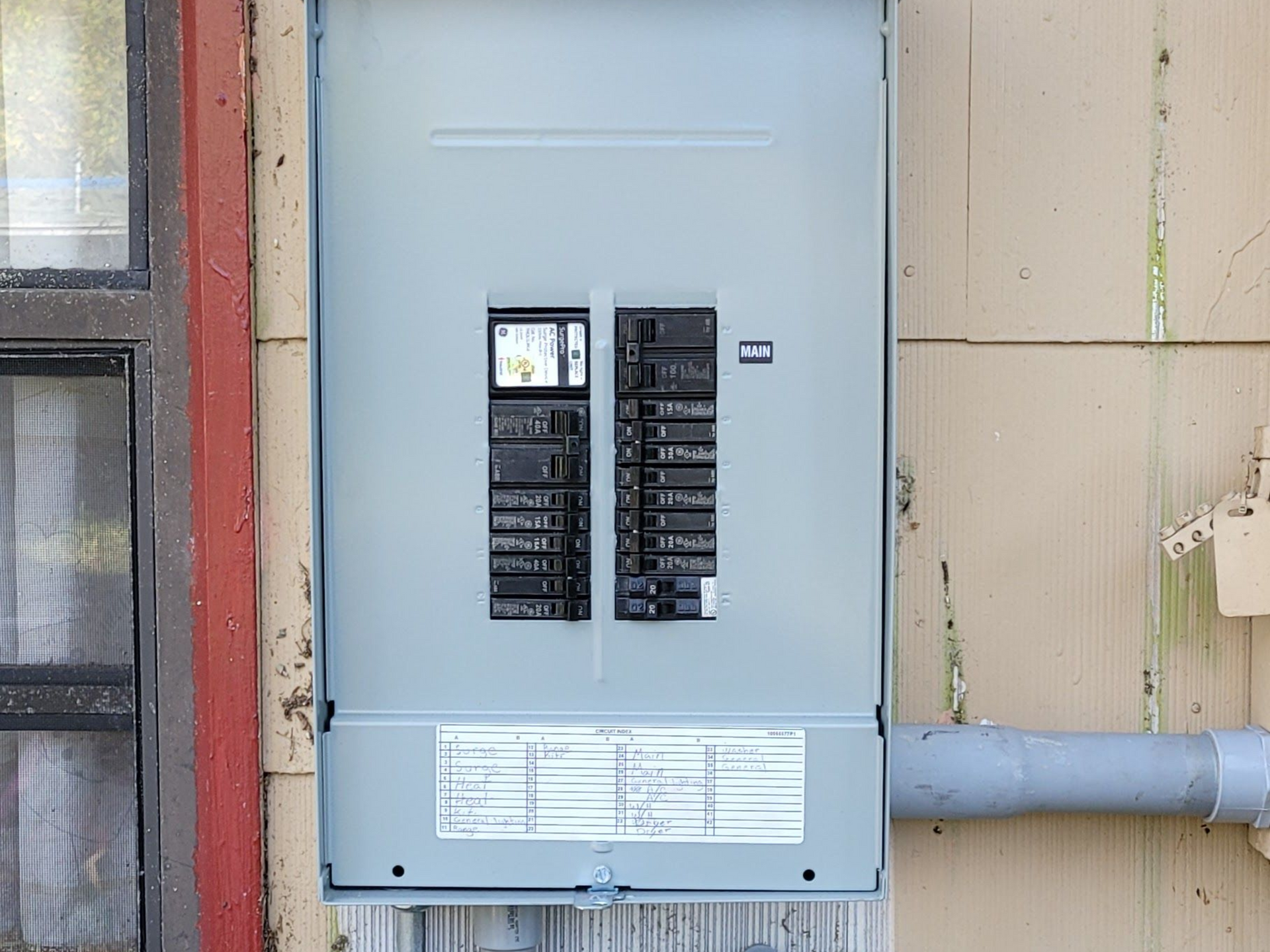 Gray electrical breaker panel and meter boxes mounted on the exterior of a beige building.