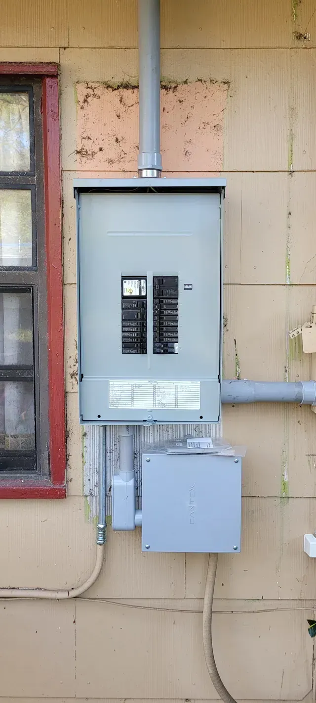 Gray electrical panels mounted on a beige exterior wall beside a red-trimmed window