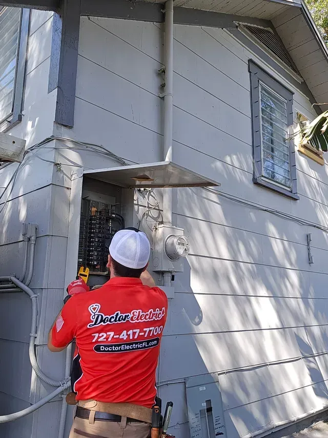 Worker in a red shirt inspecting siding on a gray house exterior with a ladder nearby