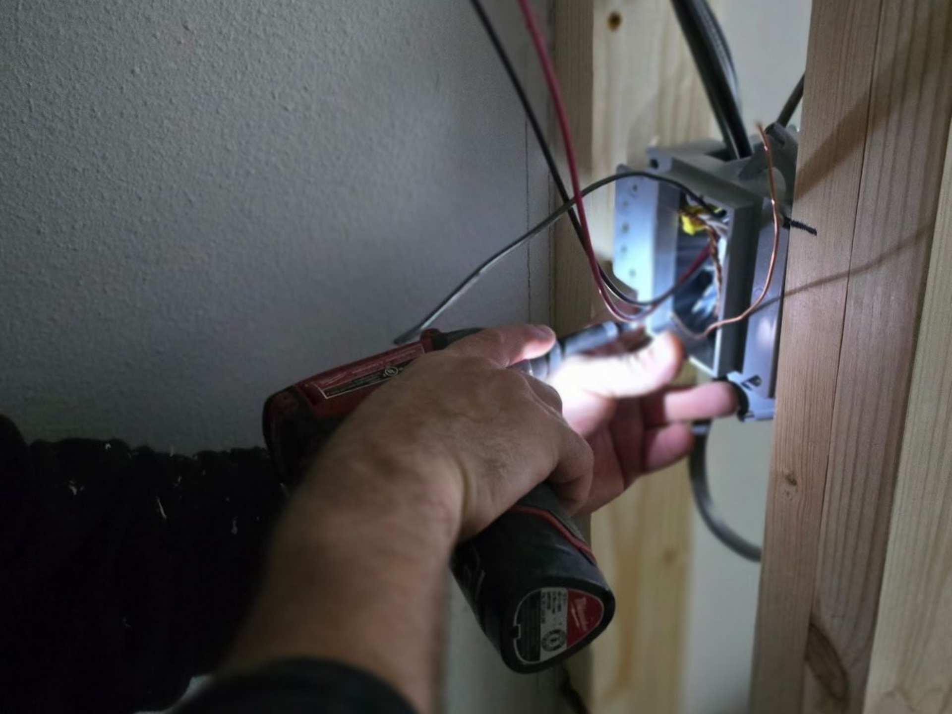 Hand wiring electrical outlet in wall cavity, with exposed red and black wires.