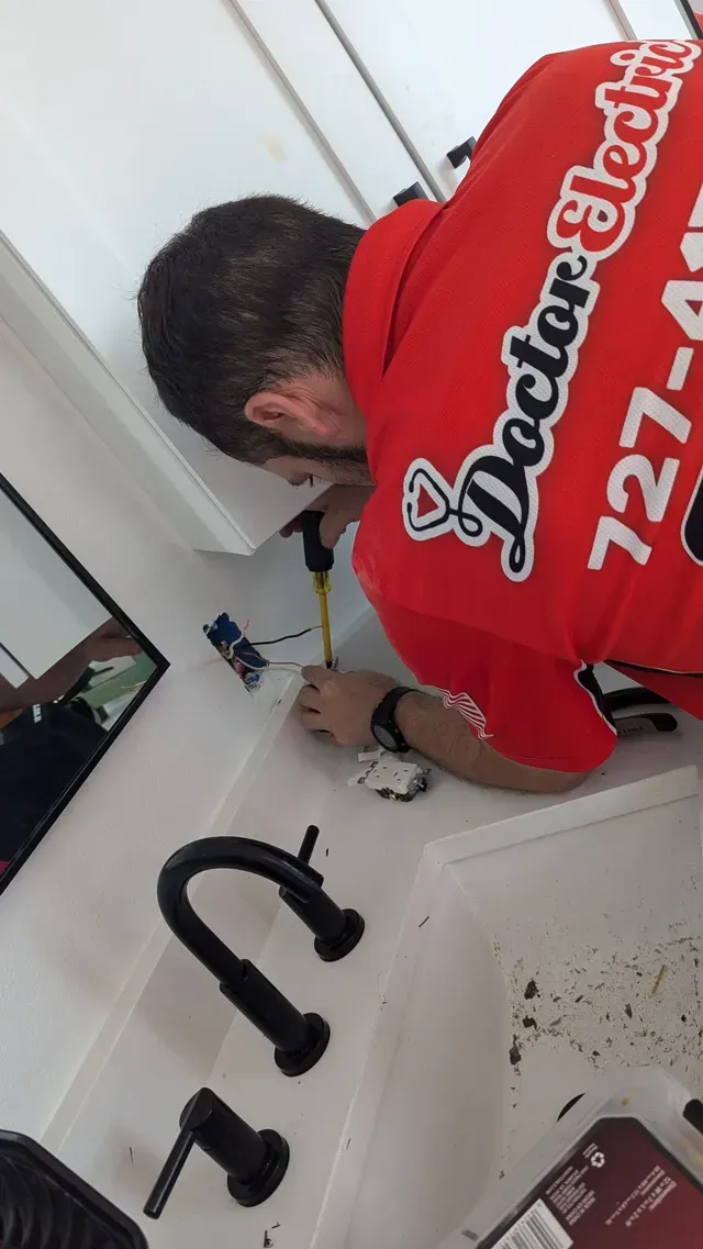 Person in a red shirt working at a kitchen sink with black faucet and white counters.