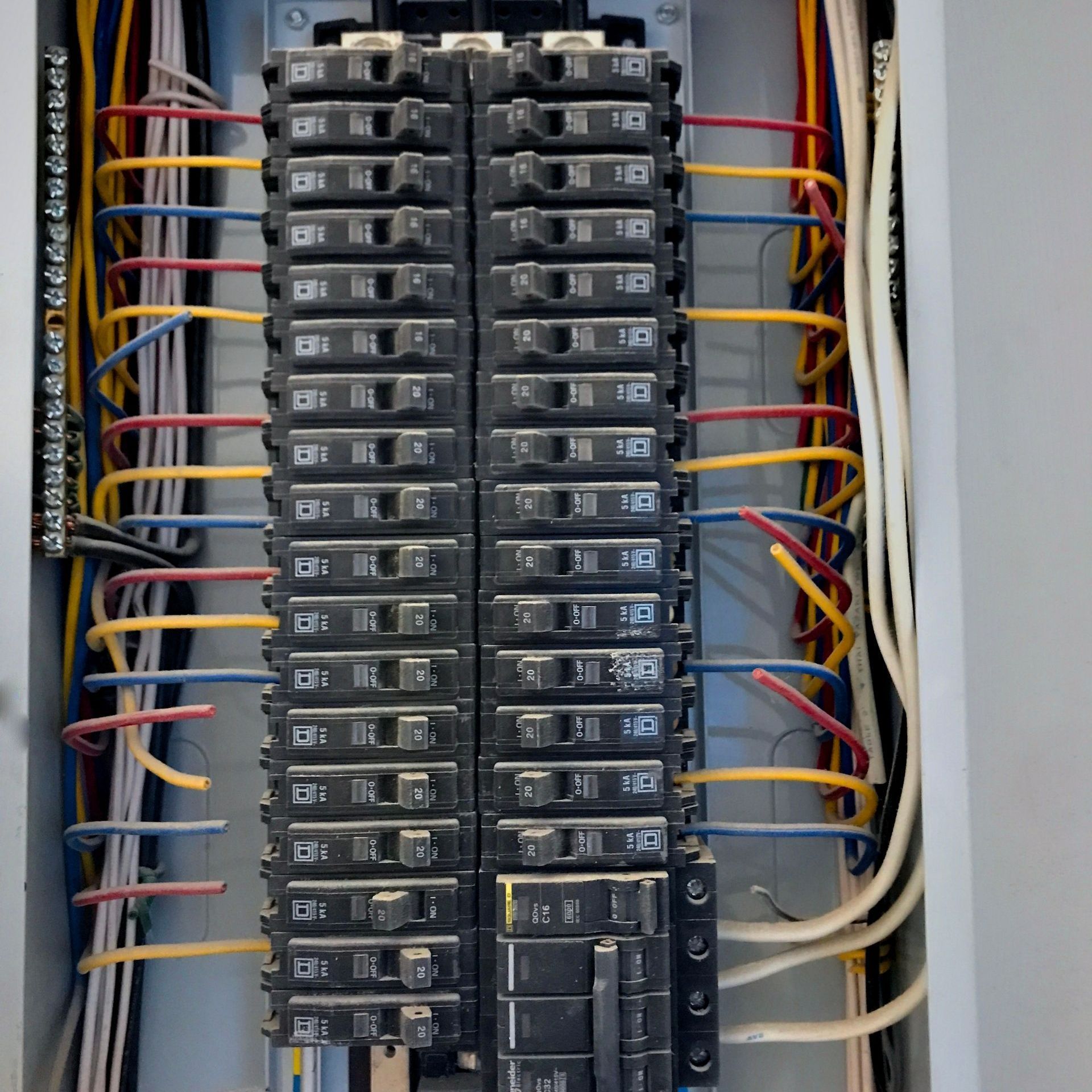 Electrical breaker panel with rows of black circuit breakers and red, yellow, and white wiring