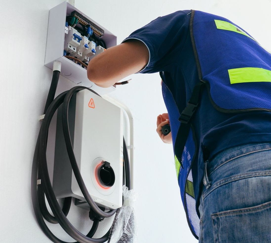 Technician installing a wall-mounted electrical unit with exposed wiring.