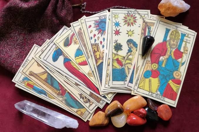 Cartas del tarot desplegadas sobre tela color burdeos con cristales y piedras a su alrededor.