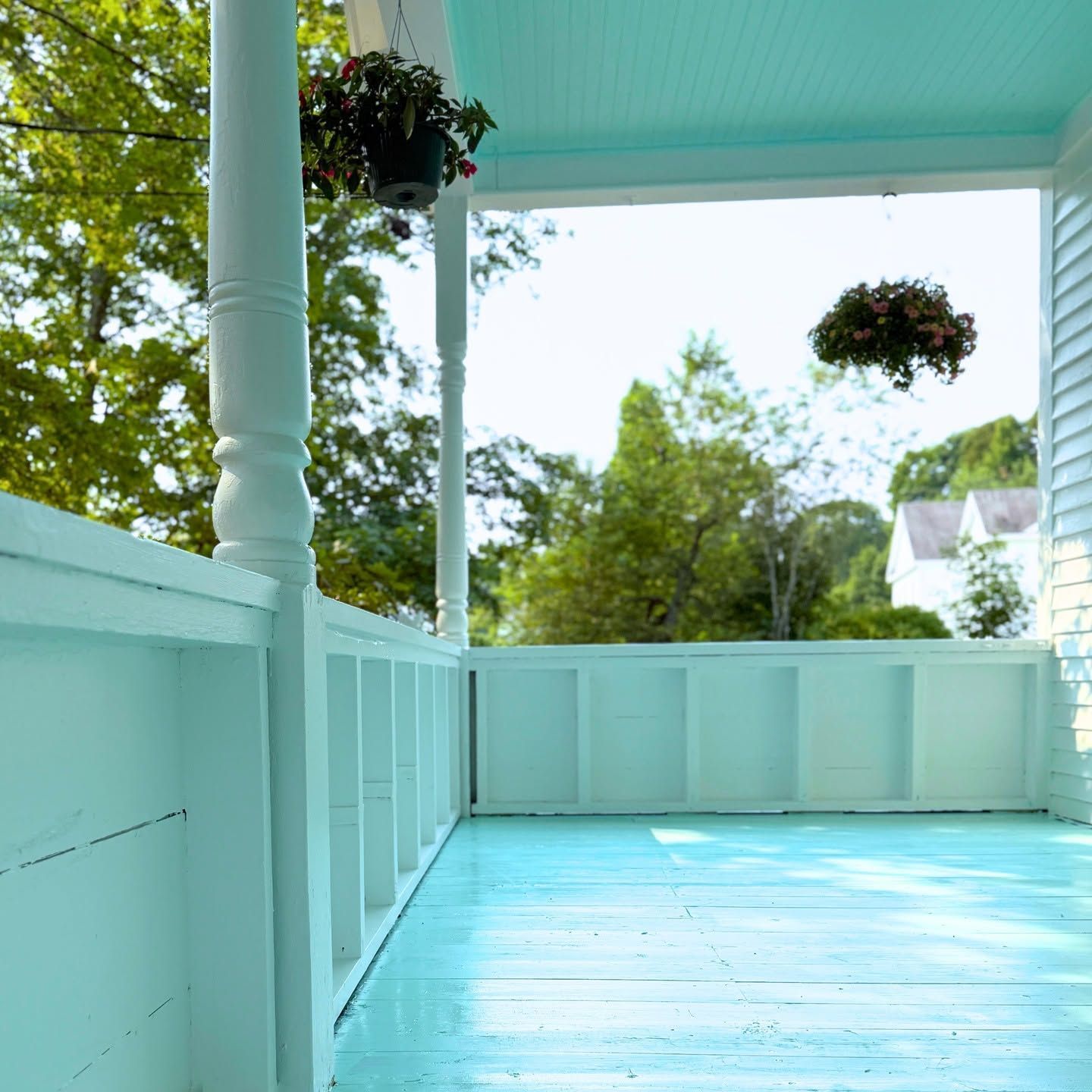 Mint-green porch with hanging flower baskets and a view of trees beyond the railing