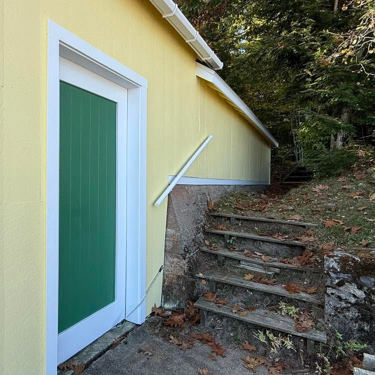 Yellow building exterior with green door and stone steps leading uphill through trees