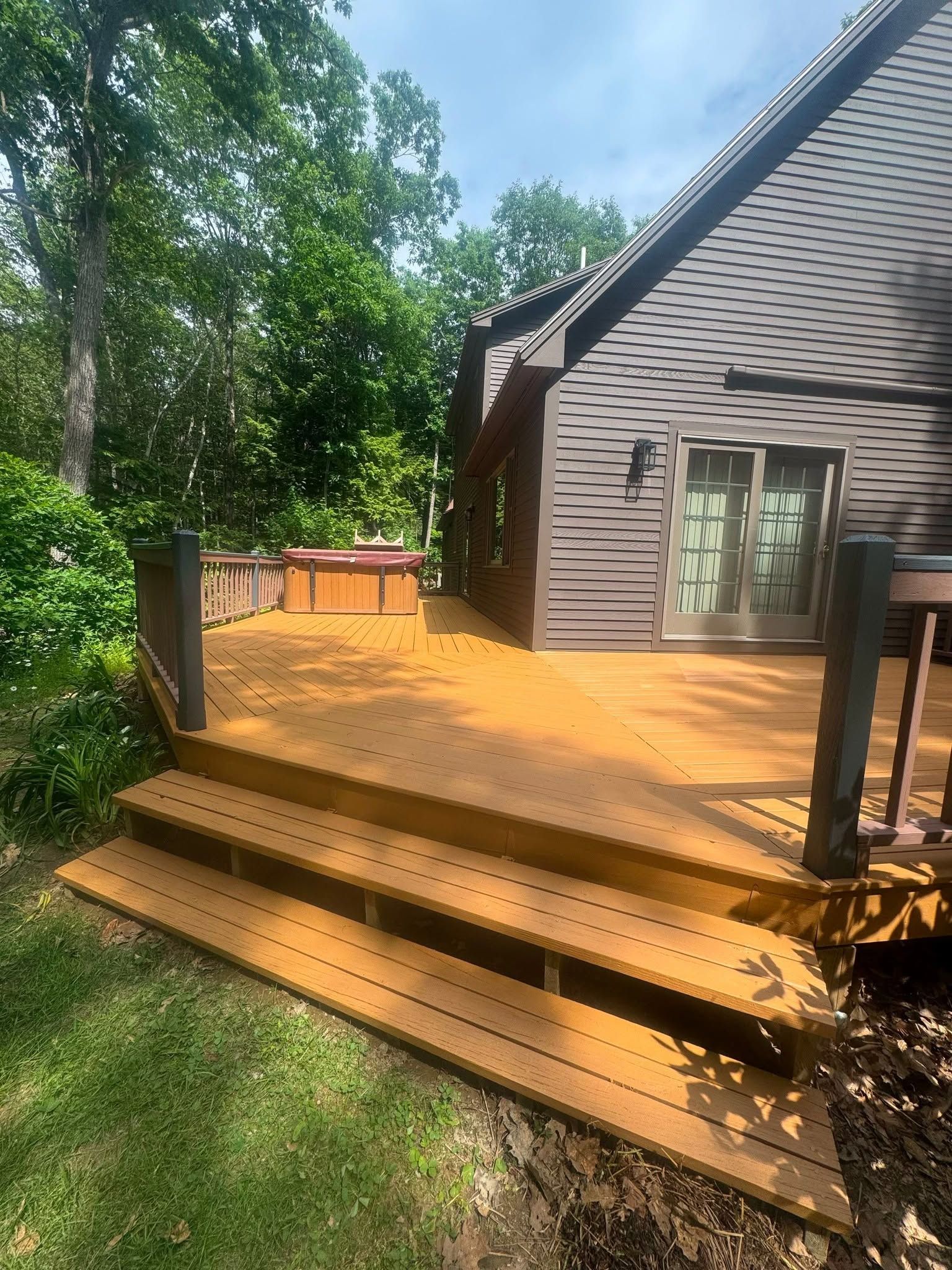 Wooden deck with steps beside a house, surrounded by trees and grass.