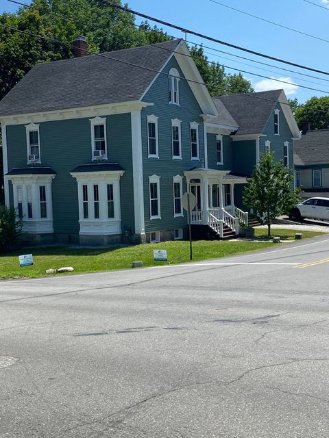 Blue two-story house on a sunny street corner with white trim and a small front porch