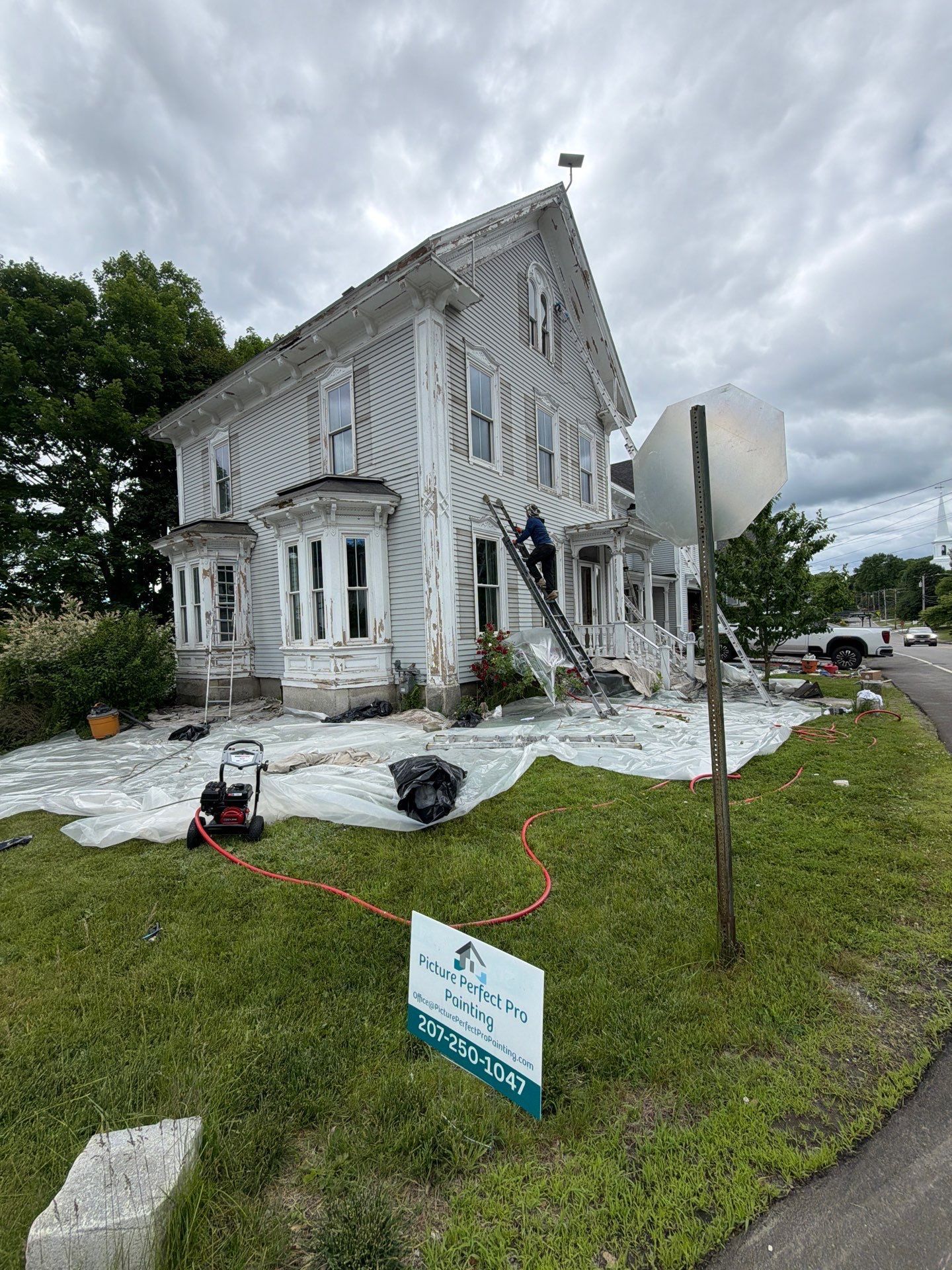 Damaged white house with debris and equipment in yard, likely after storm or renovation.