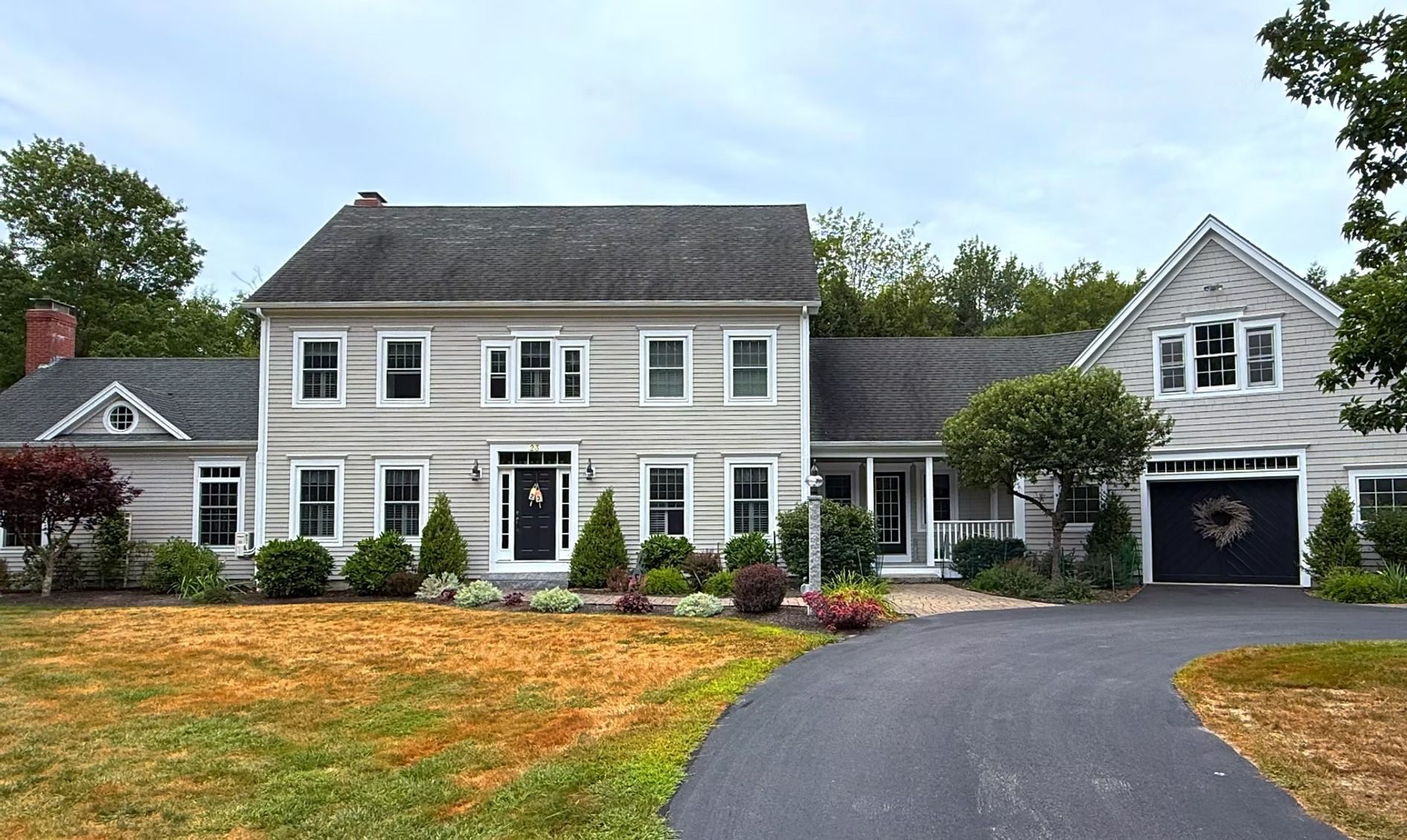 White two-story suburban house with black shutters, attached garage, and curved driveway in front lawn
