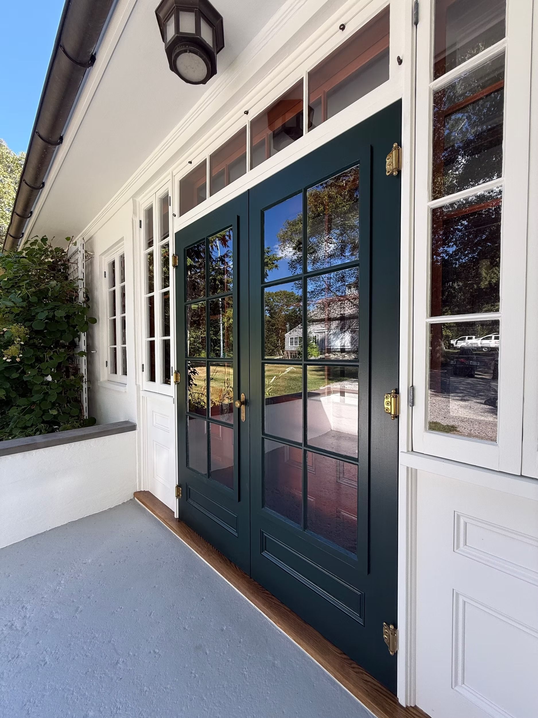 Dark green double front doors with glass panes and white trim on a covered porch