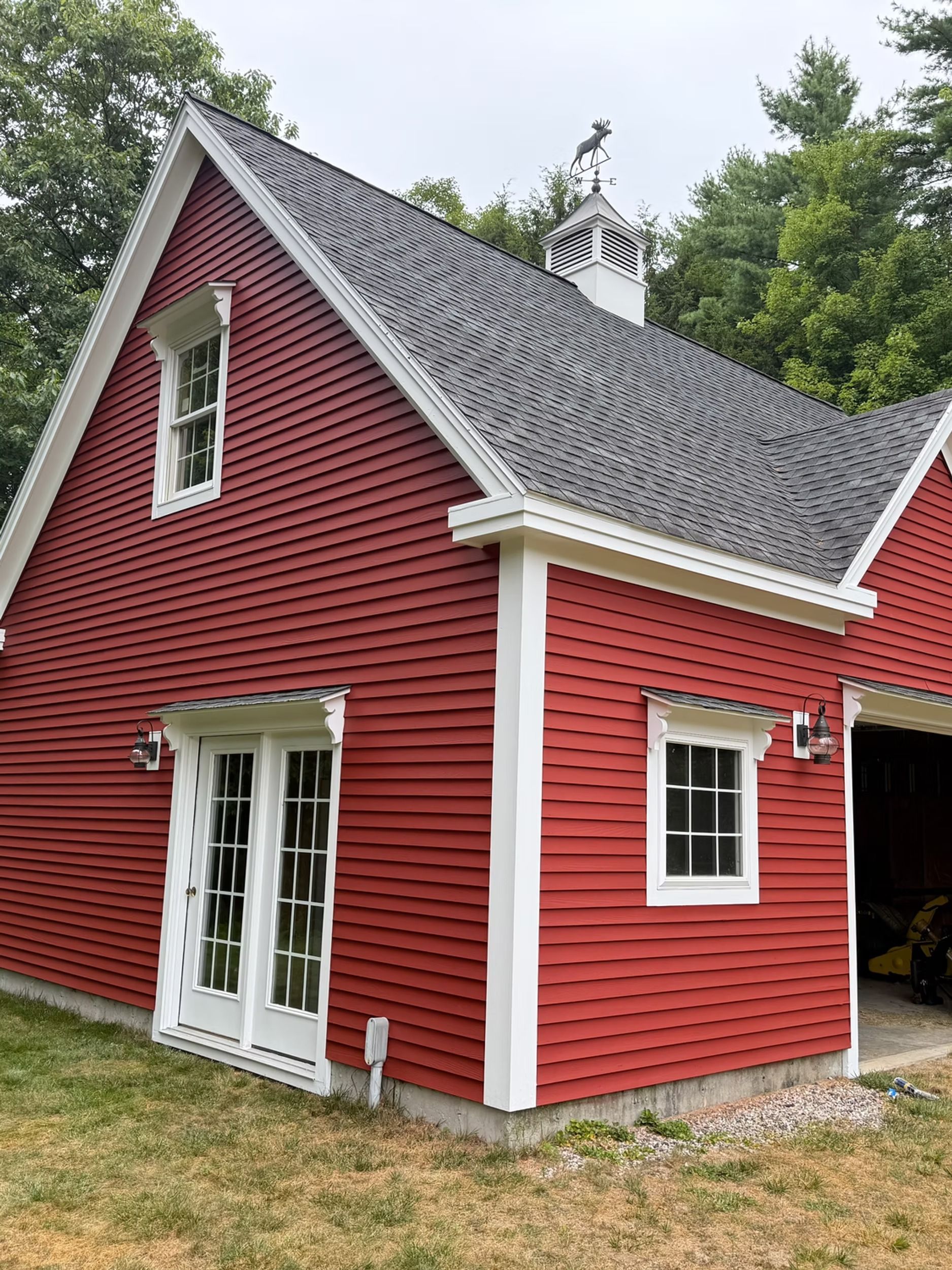Red clapboard house with white trim, steep gray roof, and double French doors amid trees