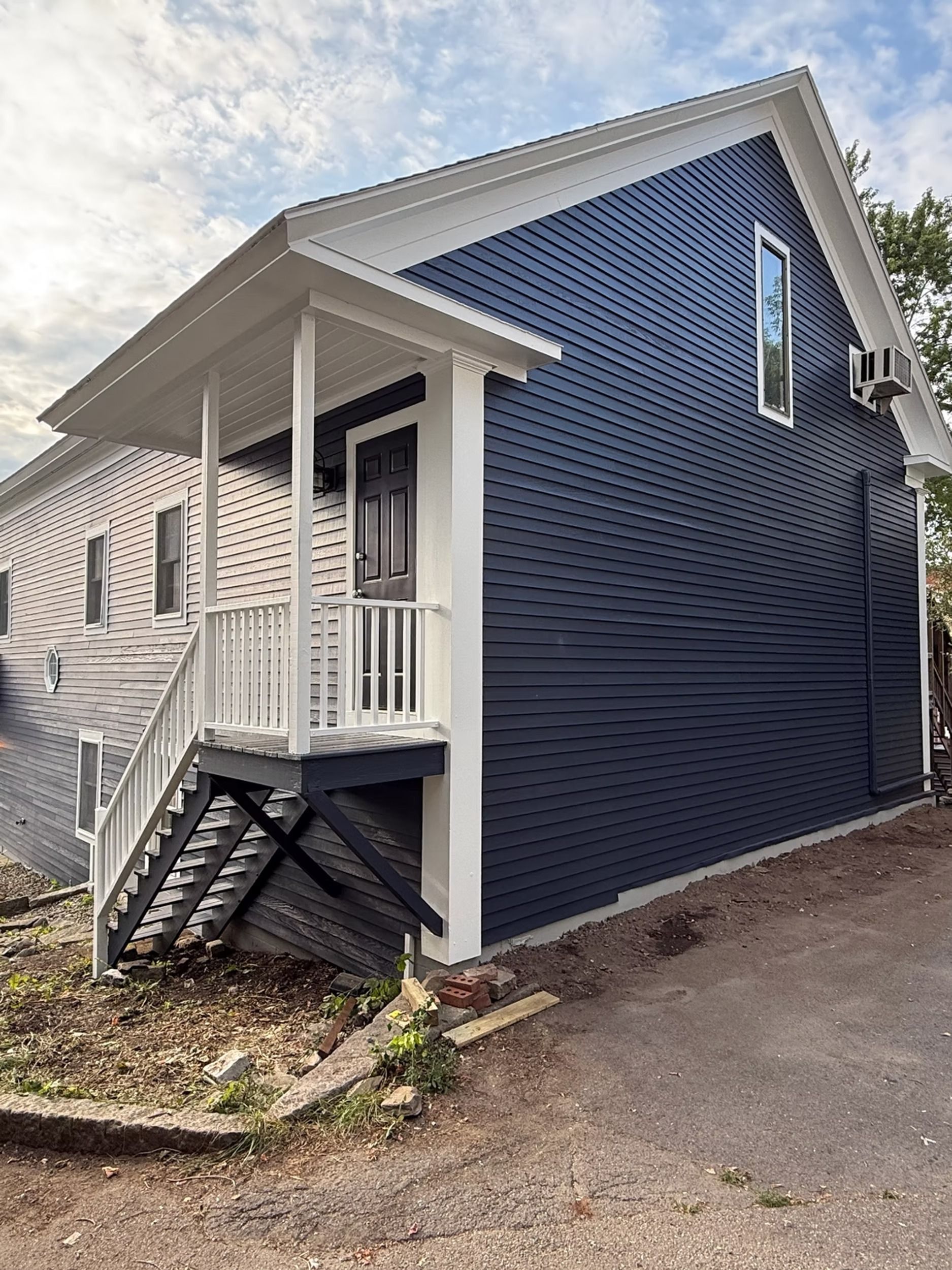 Blue-sided house with small front porch, white trim, and stairs beside a gravel drive