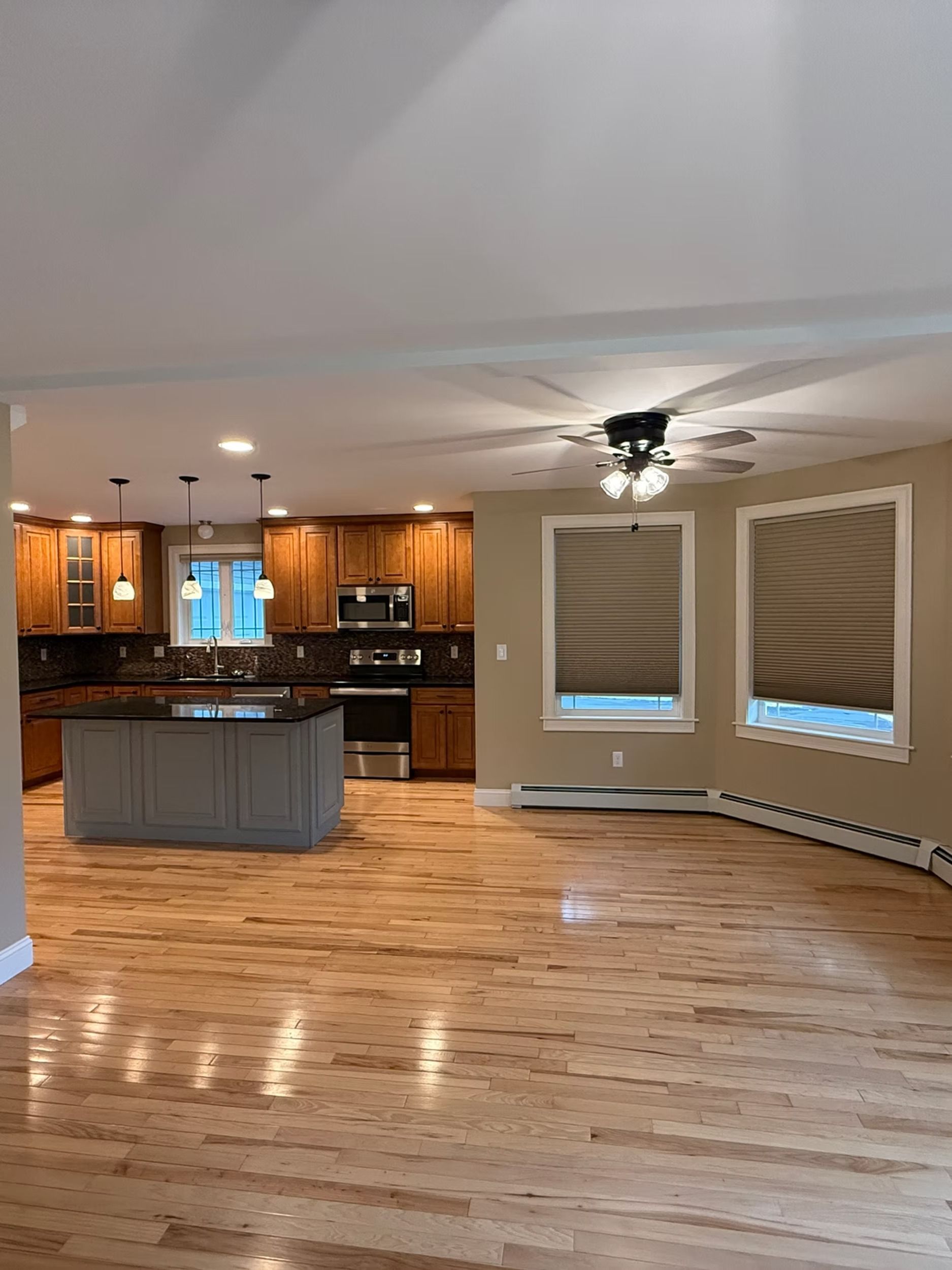 Spacious open-plan kitchen and living area with hardwood floors, gray island, wood cabinets, and ceiling fan.