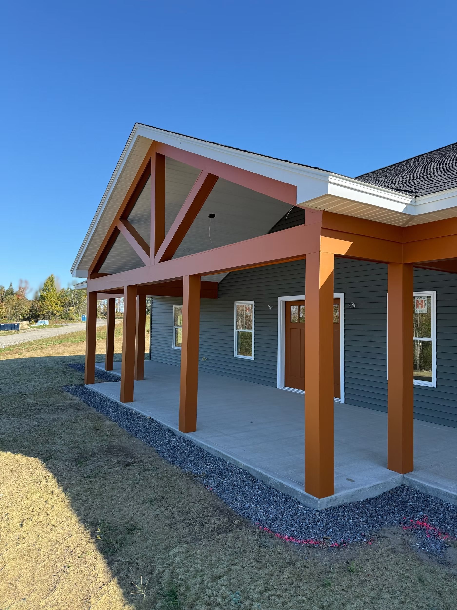 Covered porch with orange wooden posts and white trim on a green house under a clear blue sky
