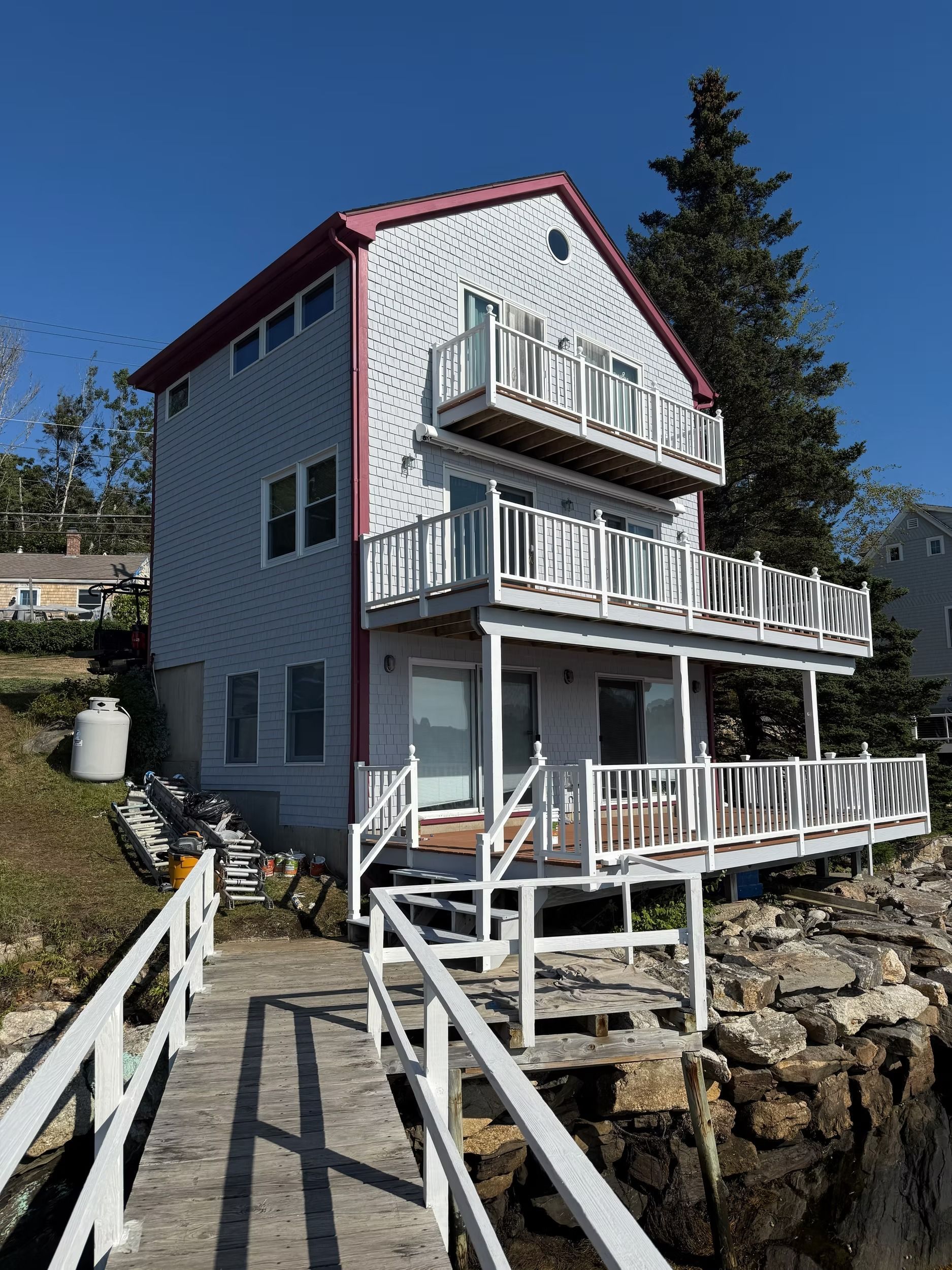 White seaside house with balconies and dock steps on a rocky shoreline under a blue sky