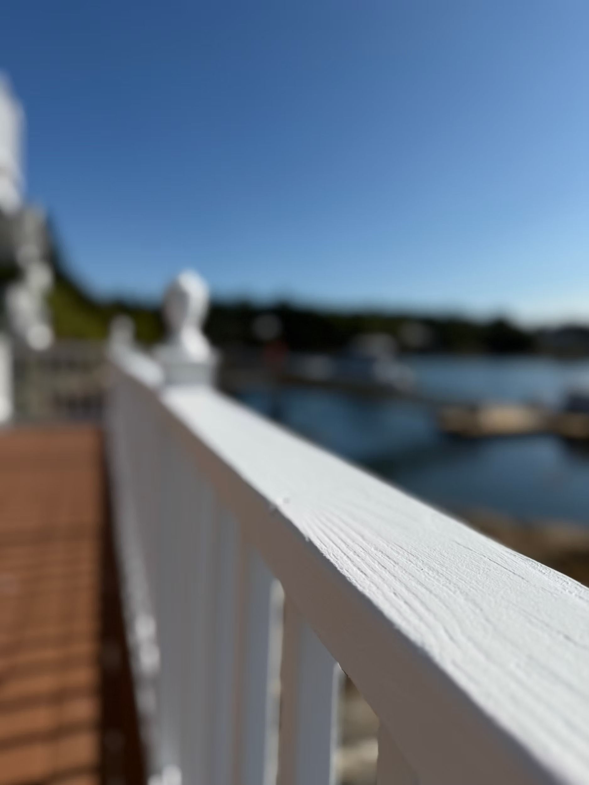 White railing leading to a calm waterfront under a clear blue sky, with a blurred dock and shoreline in the background