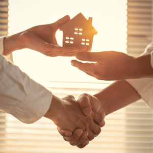 Hands shaking beneath a glowing house model in a warm office setting