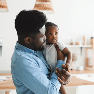 Adult holding a baby in a bright home, both looking off to the side.