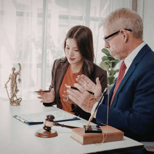 Two businesspeople reviewing documents at a desk with a gavel and microphone in a bright office