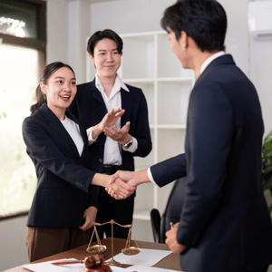 Business people shaking hands in an office while a colleague applauds nearby