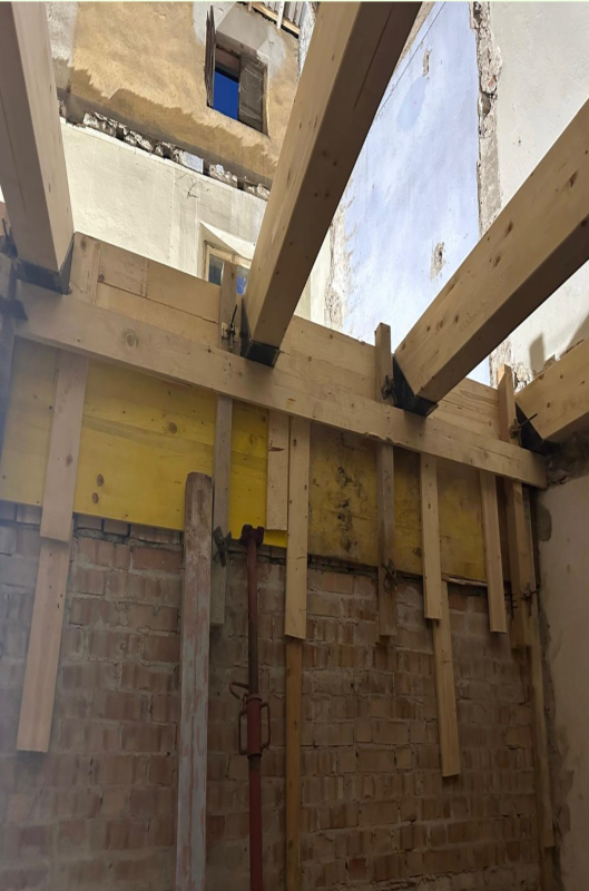 Travi del tetto in legno a vista sopra un muro di mattoni in una stanza parzialmente demolita