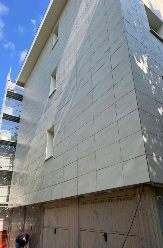 Esterno di un edificio moderno con facciata piastrellata di bianco e cielo azzurro, attualmente in costruzione al piano terra.