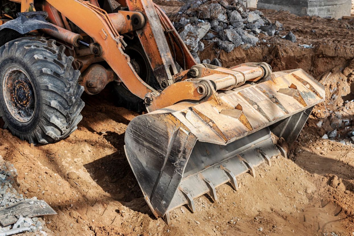 La benna arancione di una terna scava in un terreno sabbioso in un cantiere.