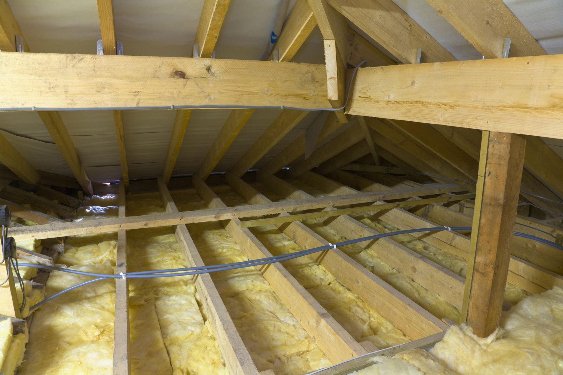 Soffitta non rifinita con travi in legno a vista e isolamento tra i travetti del pavimento.