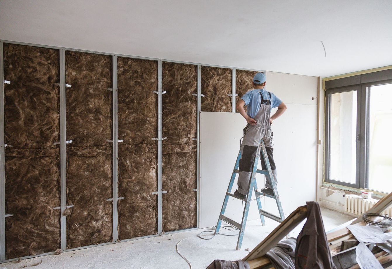 Operaio su una scala che installa materiale isolante in una stanza in fase di ristrutturazione.