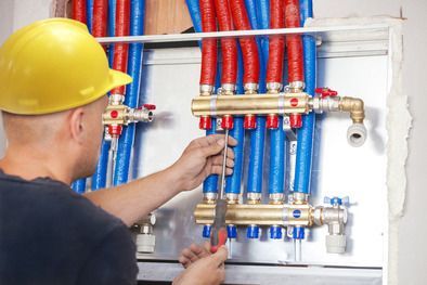 Idraulico con elmetto giallo che regola tubi rossi e blu in un quadro di distribuzione a parete.