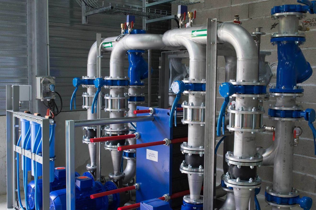 Tubazioni industriali e valvole blu in un impianto meccanico, con serbatoi e attrezzature in acciaio inossidabile.