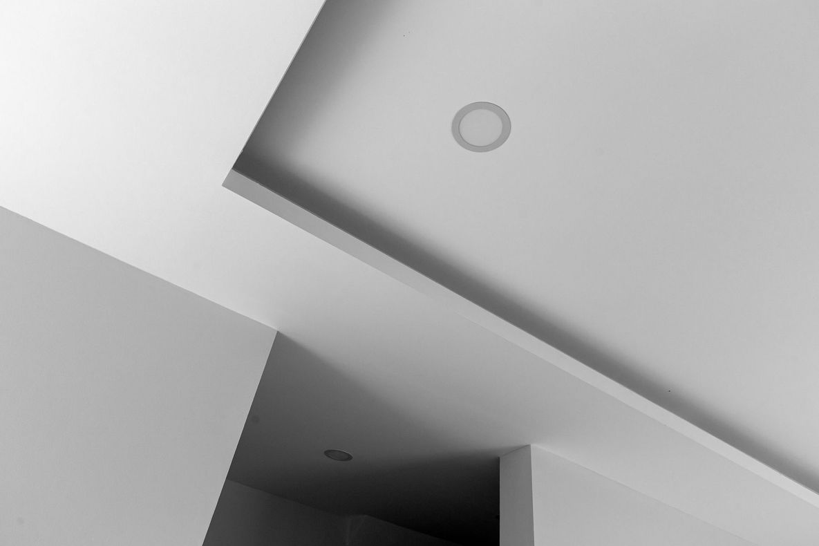 Soffitto interno con travi bianche angolate e lampadario rotondo a incasso.