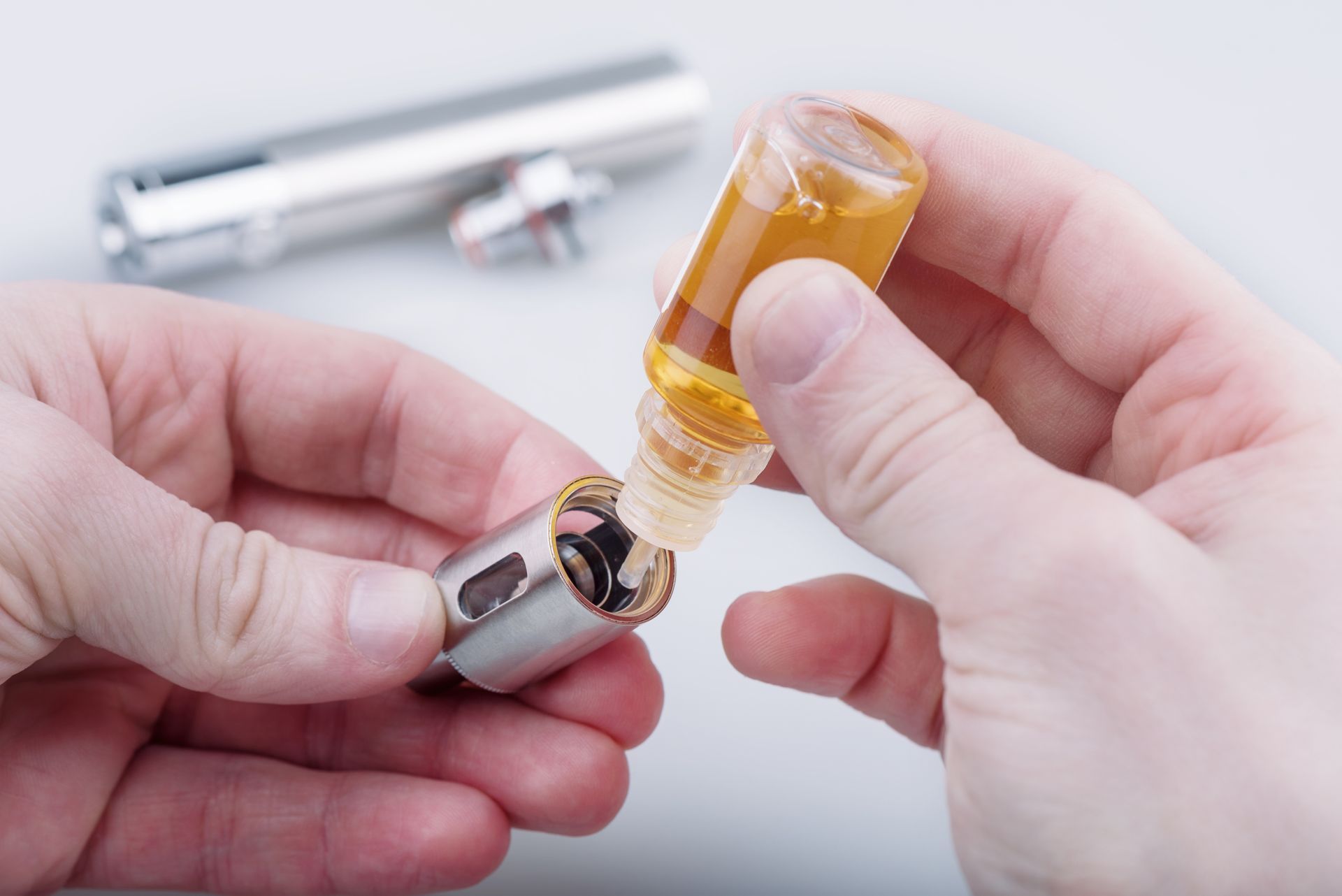 Hands filling a clear vape cartridge with amber liquid using a syringe