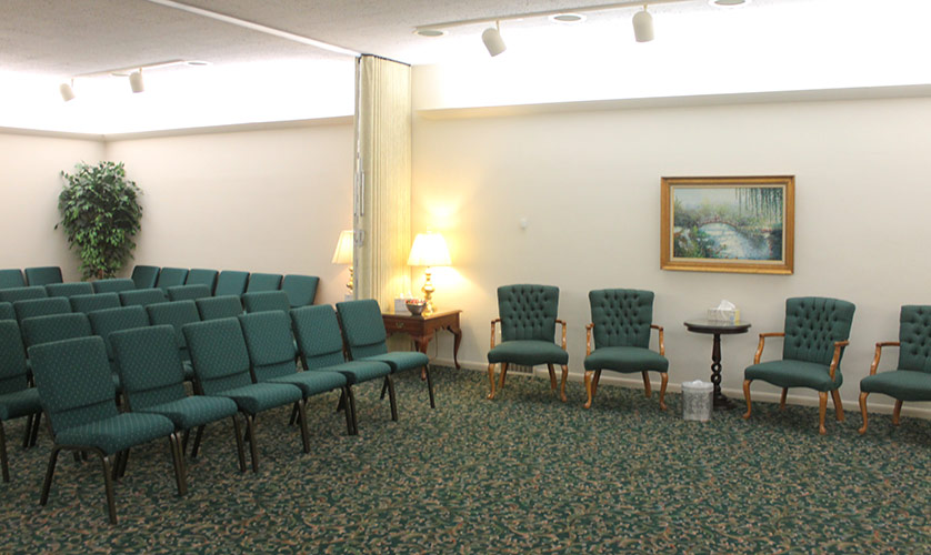 Waiting room with green chairs, patterned carpet, a side table lamp, and framed wall art.